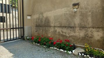 Een toegangspoort met een betonnen muur, een grindpad en een bloembed met rode bloemen.
