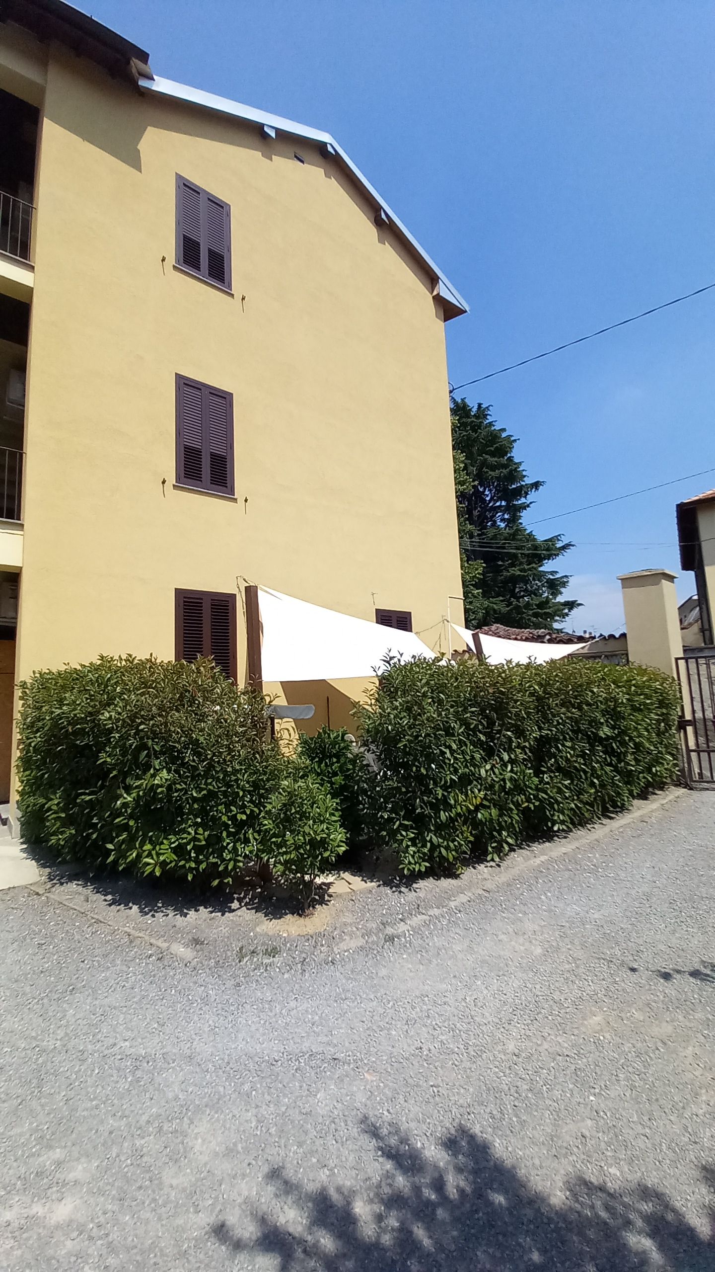 Un edificio a due piani con facciata piatta, diverse finestre con persiane e un vialetto sterrato.