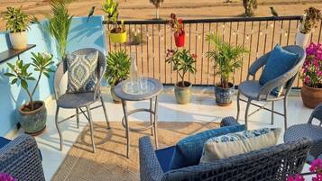 A balcony with wicker furniture, potted plants, and a view of the beach.