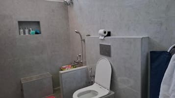 Un baño con inodoro, ducha y un estante pequeño con artículos de aseo.