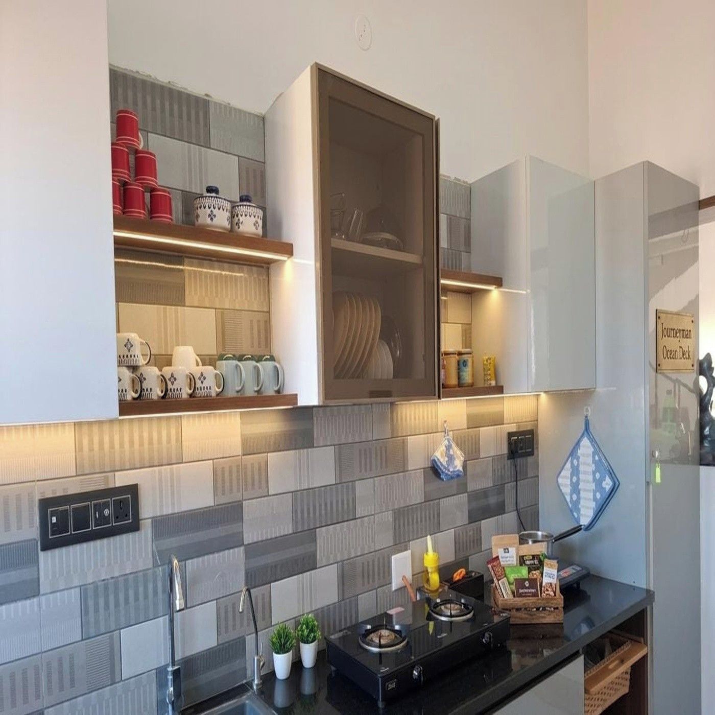 A modern kitchen with a built-in stove, a microwave, and a range hood. There are cabinets above the counter with various kitchen items.