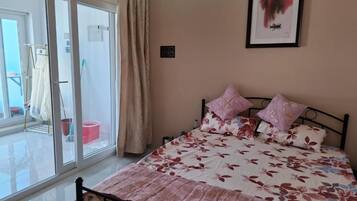 A bedroom with a bed, a window, and a door leading to a balcony.
