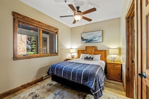 Una camera da letto con un letto, una ventola a soffitto, una finestra, un quadro e un comodino con una lampada.
