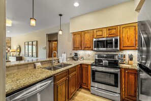 A modern kitchen with granite countertops, stainless steel appliances, wooden cabinets, and pendant lighting. - Steps to the Lifts | Hot Tubs, Fireplace & Shuttle (Steamboat Springs)