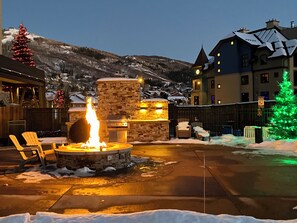 A patio with a stone fire pit, outdoor seating, and a view of a snowy mountain. - Steps to the Lifts | Hot Tubs, Fireplace & Shuttle (Steamboat Springs)