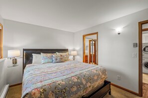 A bedroom with a bed, two bedside lamps, a mirror, and a washing machine in the corner. - Cozy 1BR Ski Condo | Fireplace + Shuttle to Slopes (Steamboat Springs)