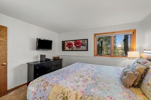Ein Schlafzimmer mit einem Bett, einem Schminktisch, einem Fernseher, einem Fenster und einem Gemälde.