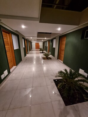 Un couloir d’hôtel aux murs verts, aux portes en bois et agrémenté de plantes en pot.