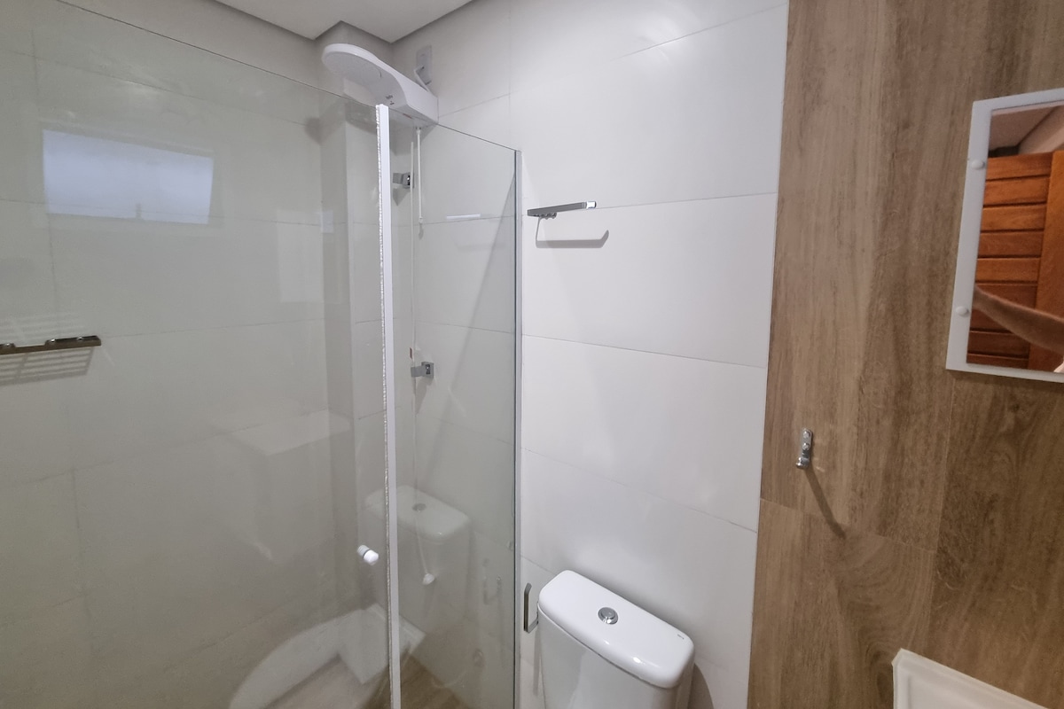 Une salle de bain avec une douche à parois de verre, des toilettes blanches et un panneau en bois sur le mur.