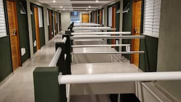 Un couloir d’hôtel avec de nombreuses chambres, chacune dotée d’une porte et d’une fenêtre avec des stores.