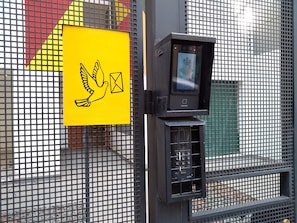 A security camera mounted on a metal fence with a yellow sign featuring a dove and an envelope.