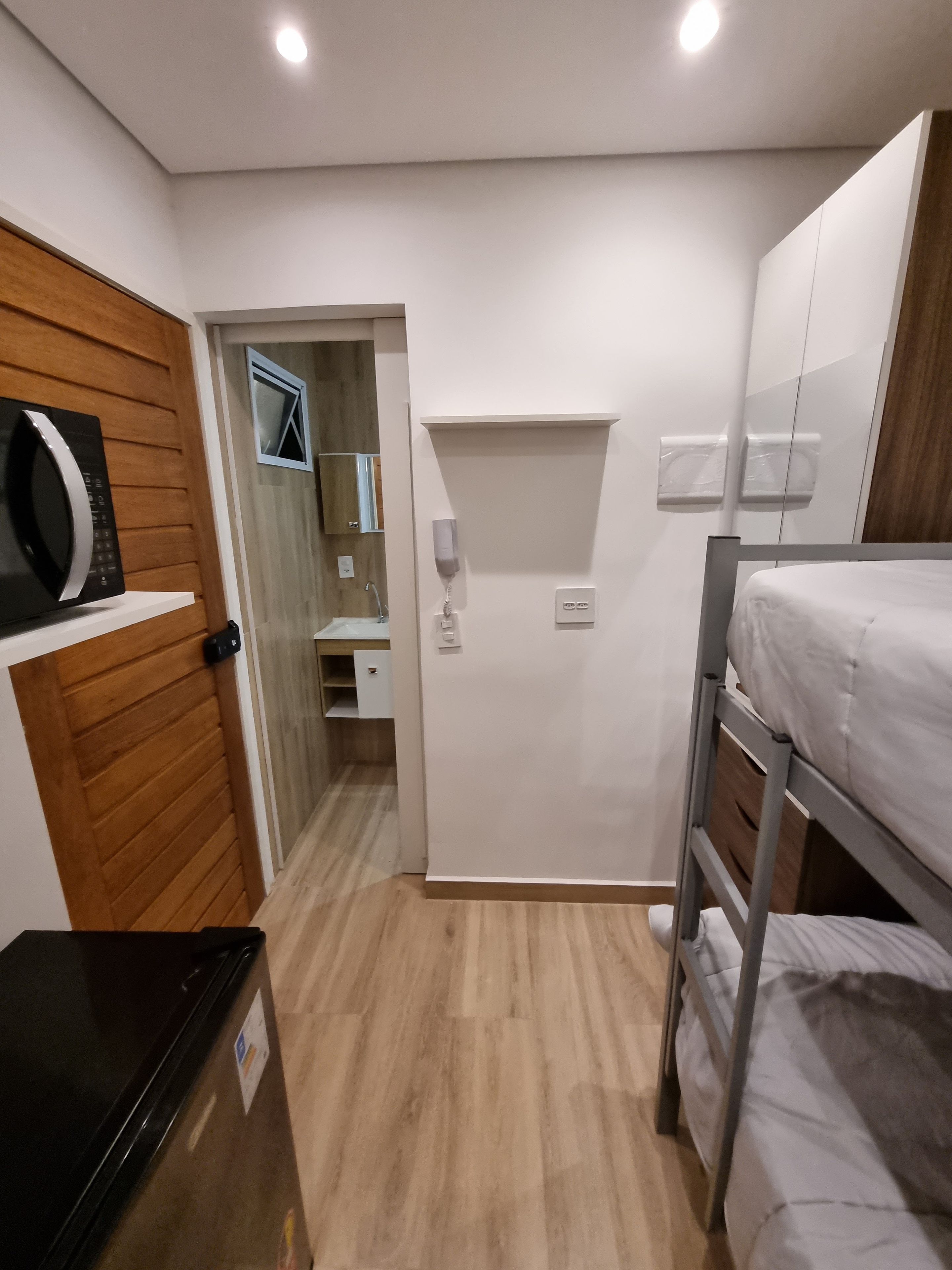 Une pièce compacte comprenant un lit superposé, un four à micro-ondes, un petit bureau et un mur recouvert de panneaux en bois.