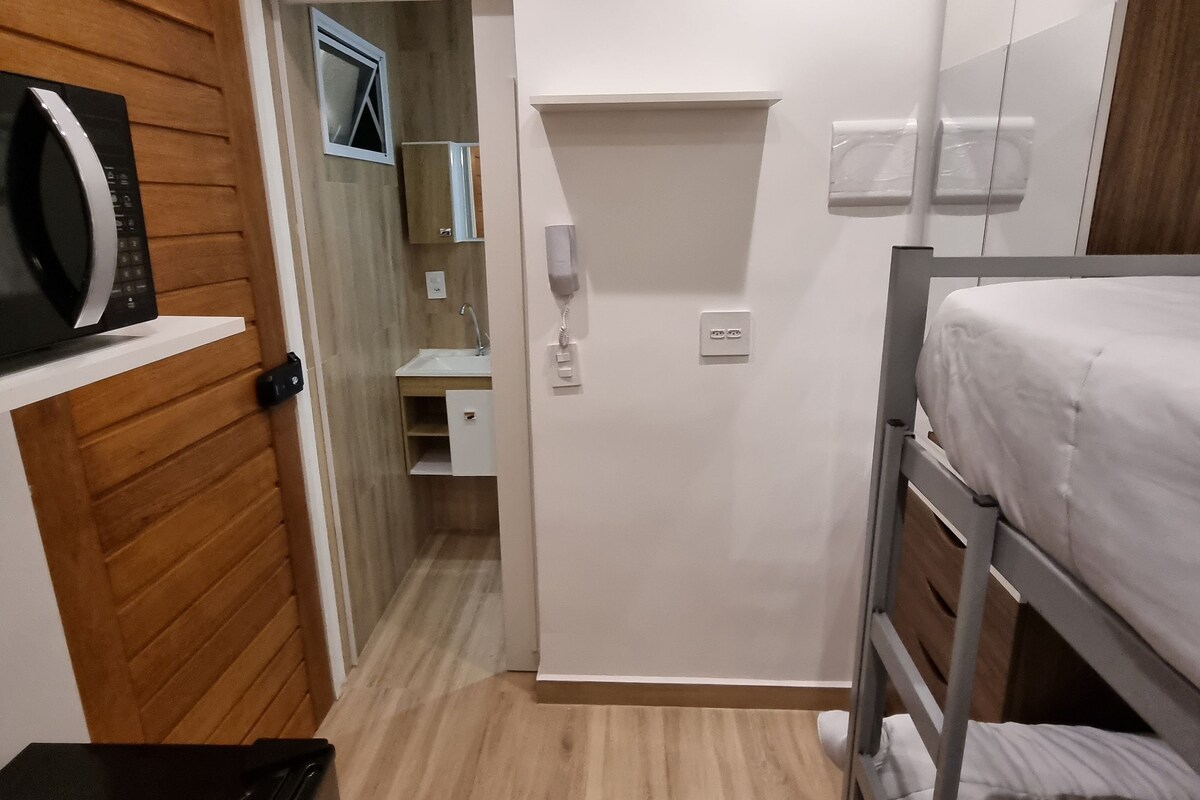 A compact room with a bunk bed, a microwave, a small desk, and a wooden panel wall.