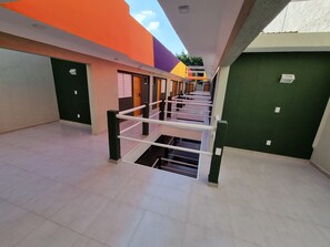 Un couloir avec une rambarde métallique, des portes et un sol carrelé.
