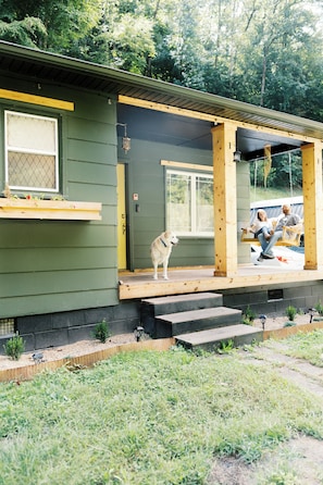 Una terraza de madera con un perro y dos personas sentadas en un columpio.