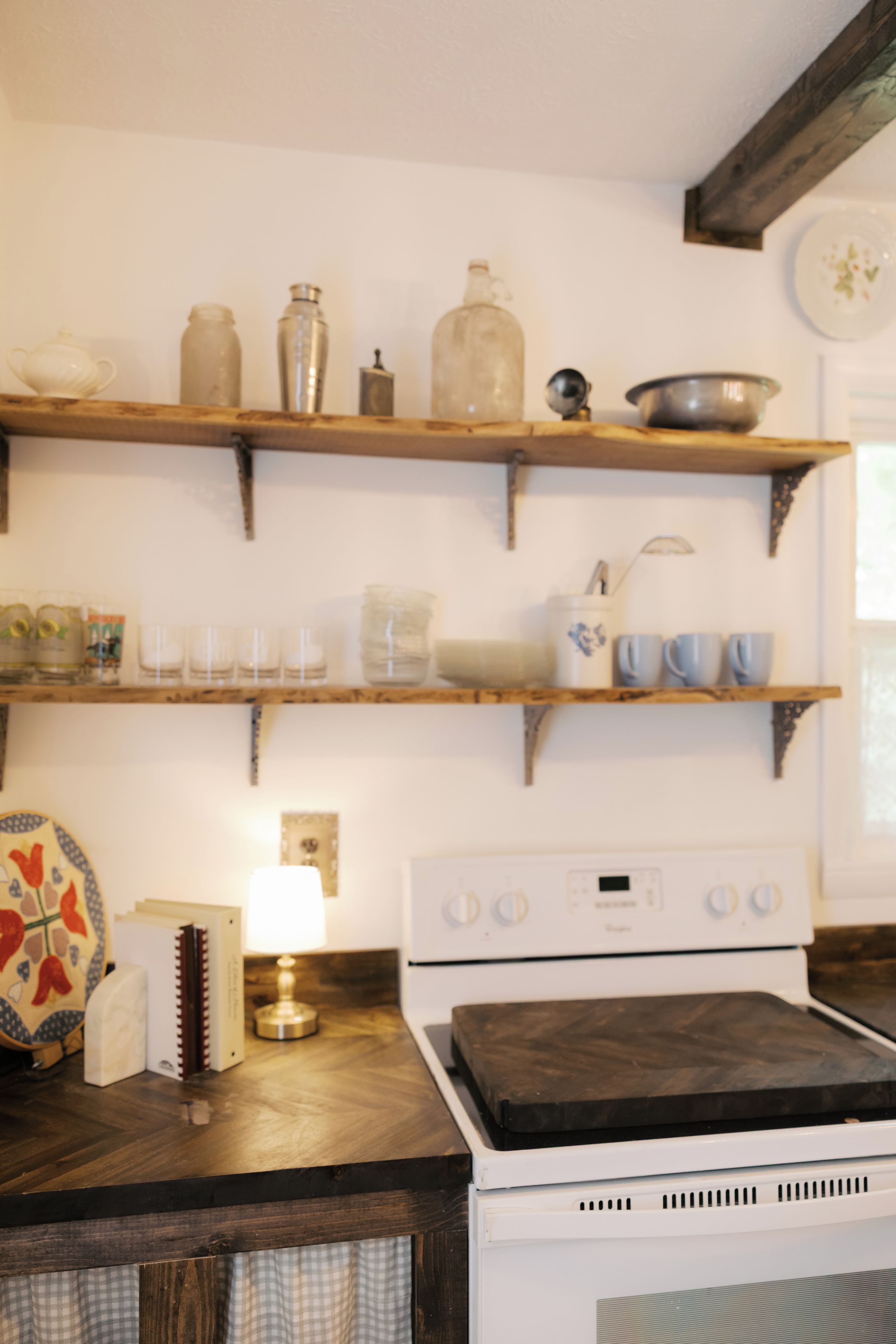 Une cuisine avec des étagères en bois où sont rangés divers ustensiles, une cuisinière et une décoration murale à motifs.