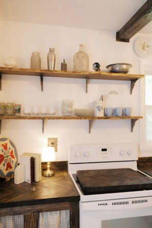 Una cucina con mensole in legno che contengono utensili da cucina, un fornello e una decorazione murale a motivi.