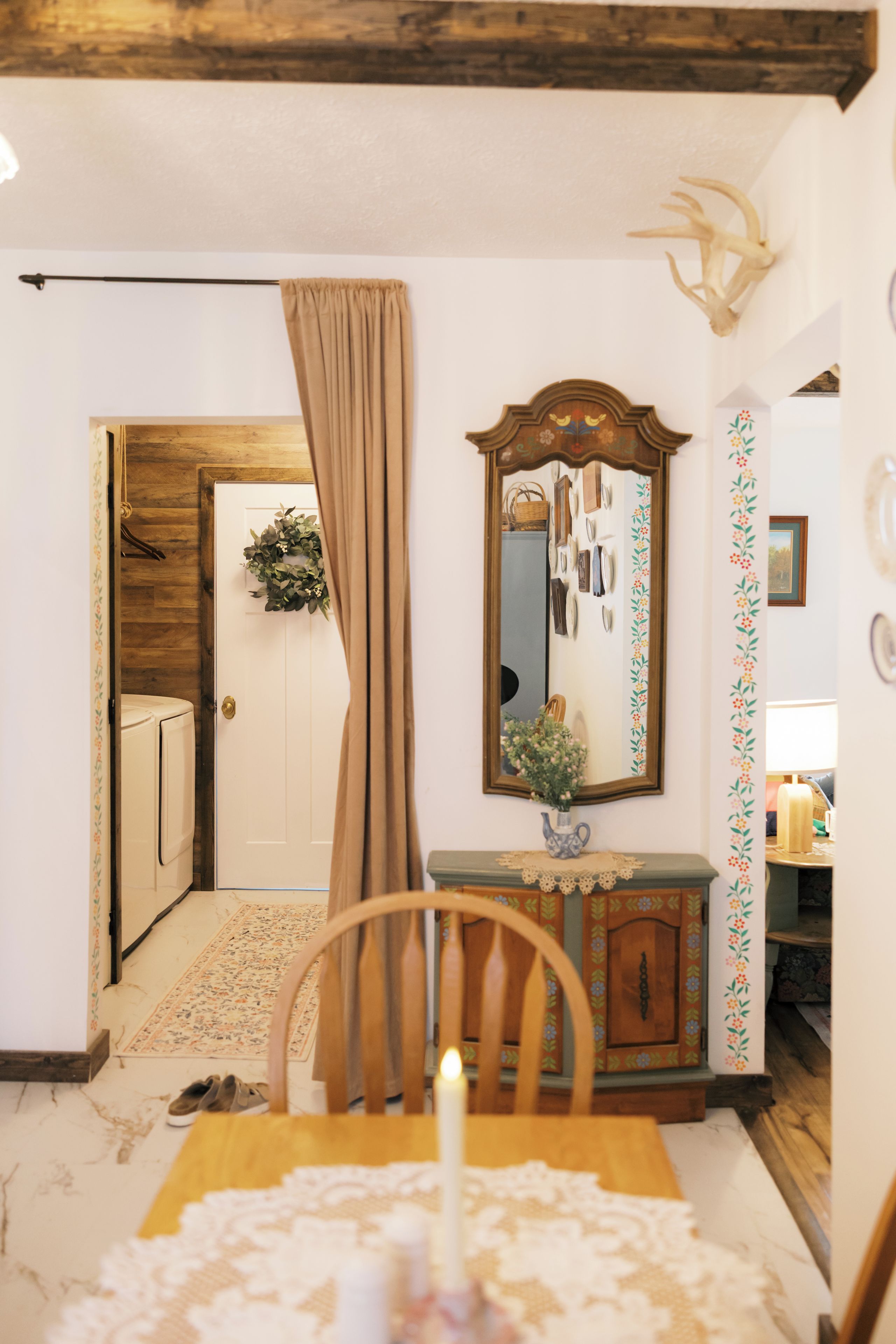 A room with a wooden door, a mirror, a vase with flowers, and a table with a lace tablecloth.