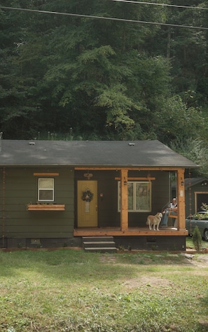 A small house with a porch, a dog, and a person sitting on a bench.
