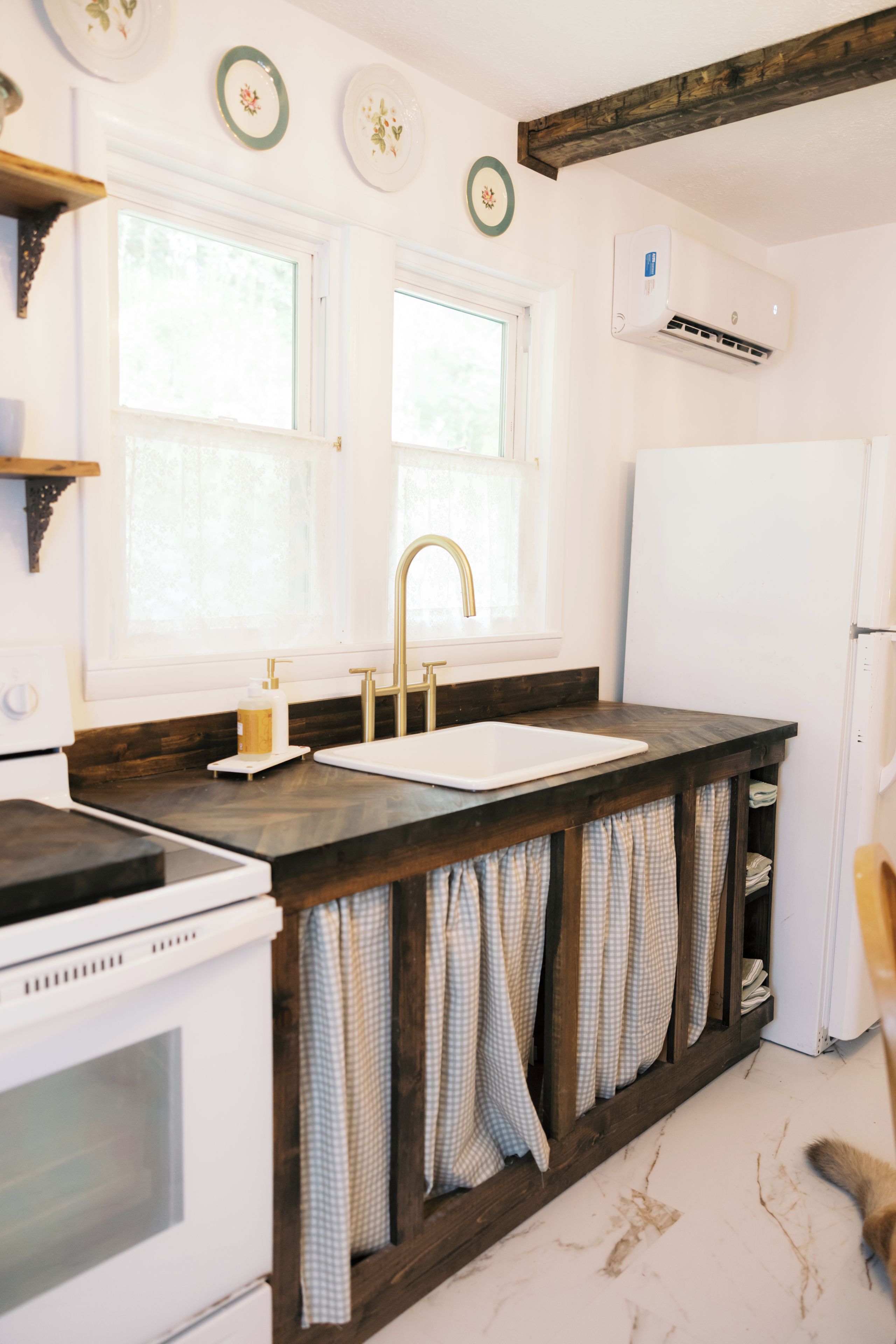 A kitchen with a white stove, a sink, and a white refrigerator. There are two windows above the sink, and a wooden beam above the stove.
