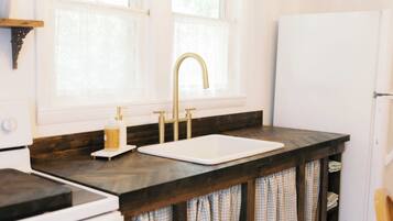A kitchen with a white stove, a sink, and a white refrigerator. There are two windows above the sink, and a wooden beam above the stove.