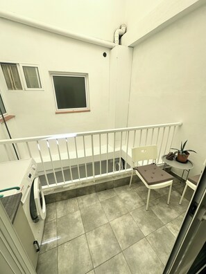 A small balcony with a white railing, a window, a chair, a table with a potted plant, and a washing machine. - Cozy Flat. Walking distance to the beach or town centre is 4 Min (Guía de Isora)