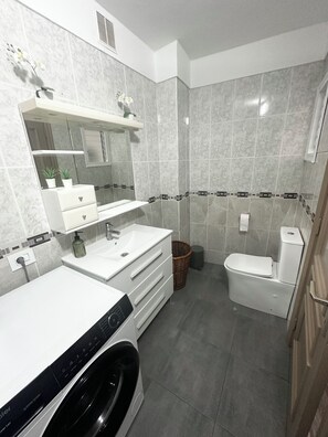 Ett modernt badrum med en tvätställsmöbel med två handfat, en toalett och en tvättmaskin.