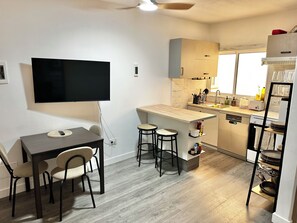 A modern kitchen with a dining area, a flat-screen TV mounted on the wall, and a window providing natural light. - Cozy Flat. Walking distance to the beach or town centre is 4 Min (Guía de Isora)