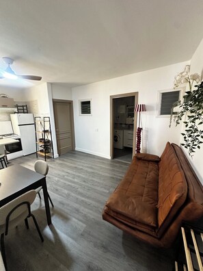 Ein kompakter Wohnraum mit einer Küchenzeile, einem Essbereich und einer Sitzecke mit einem braunen Sofa.