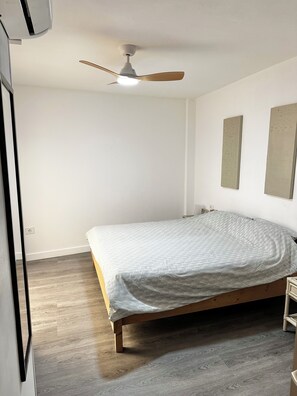 A bedroom with a bed, wooden floor, a ceiling fan, and two wall-mounted artworks. - Cozy Flat. Walking distance to the beach or town centre is 4 Min (Guía de Isora)