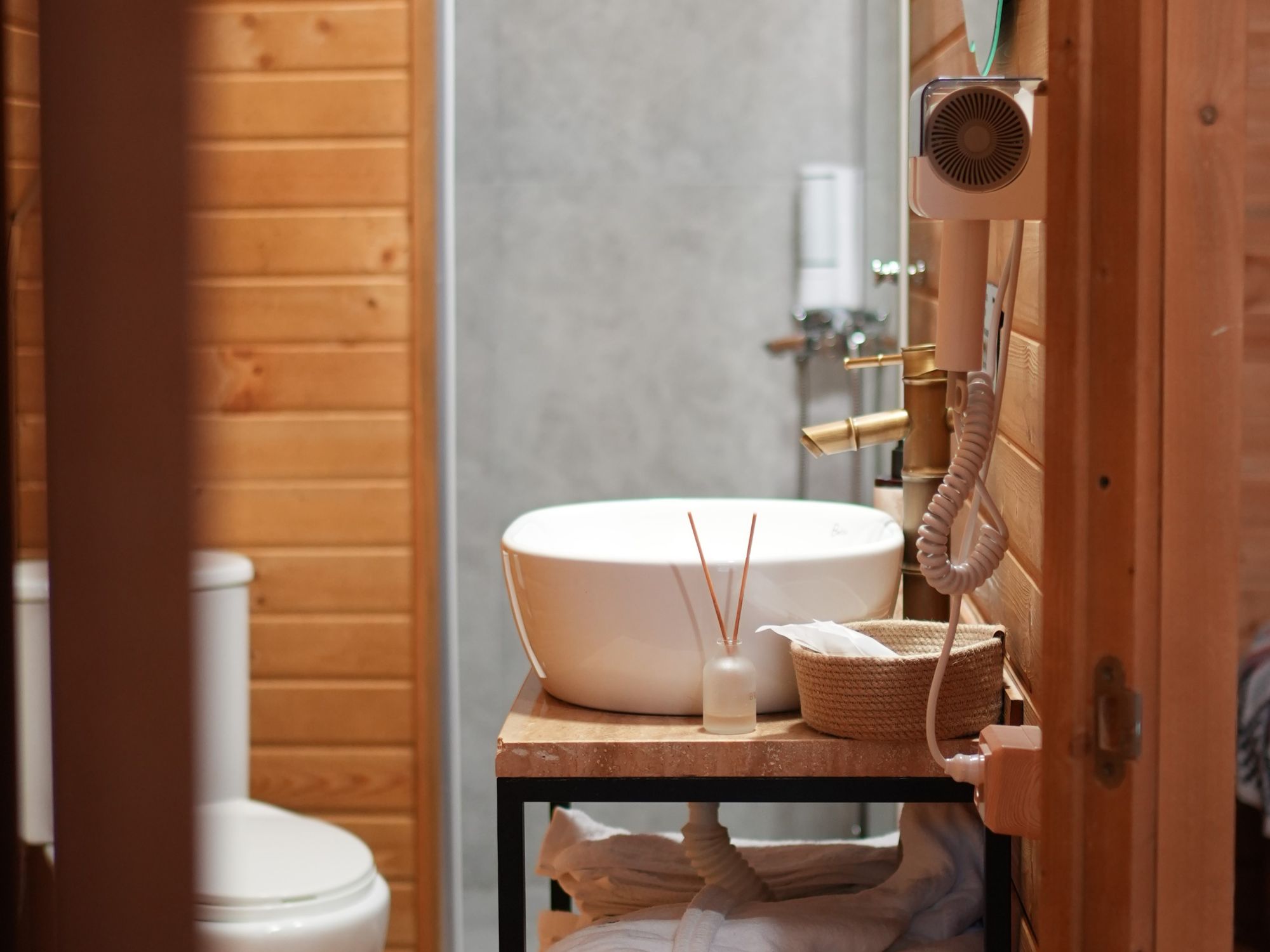 Un baño con detalles de madera, un lavamanos blanco, un abanico de mano y una pequeña cesta tejida.