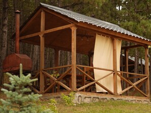 A wooden gazebo with a metal roof, surrounded by trees.