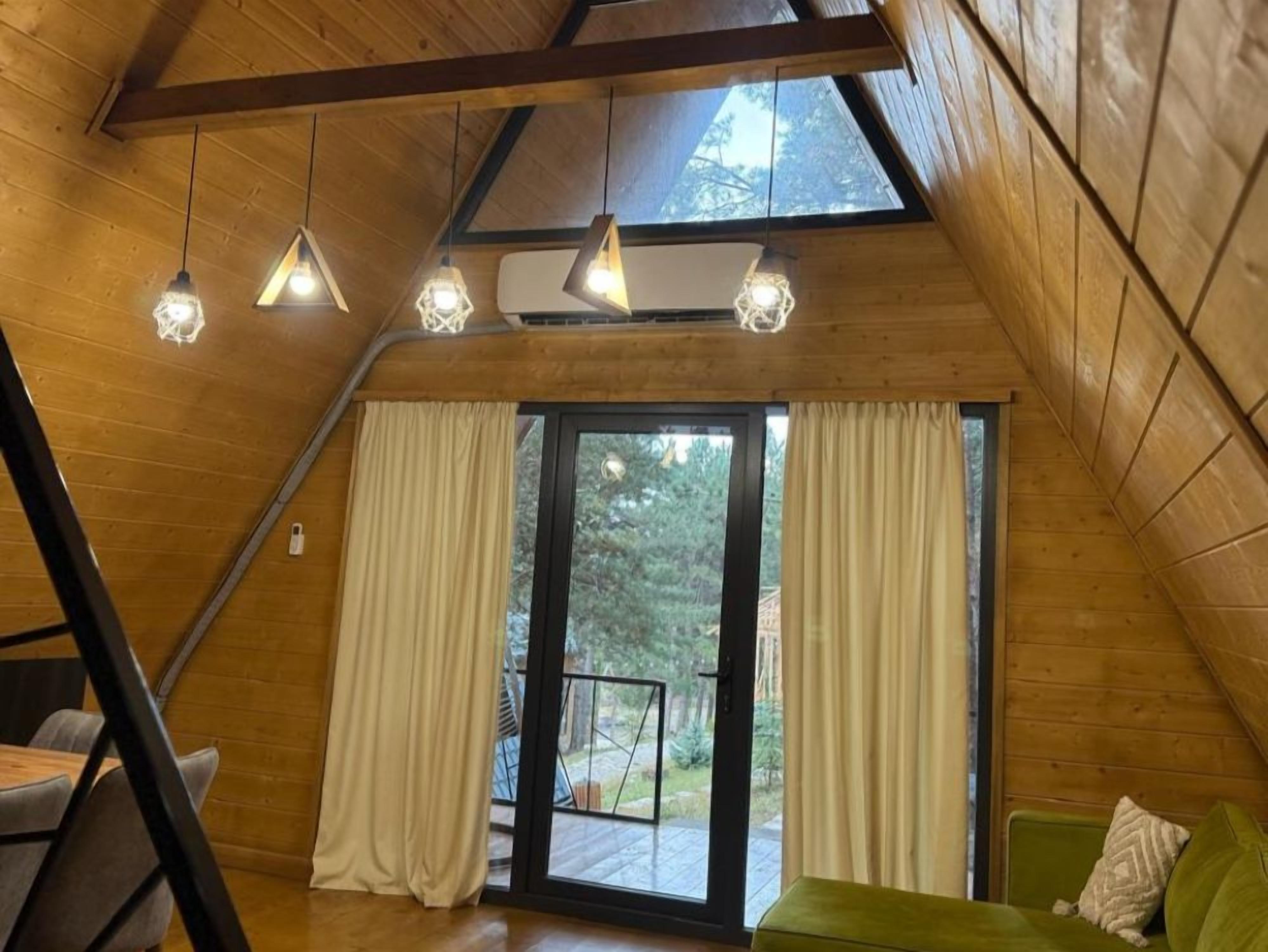 Una habitación con techo inclinado, paredes de madera, puerta corredera de vidrio y un sofá verde.
