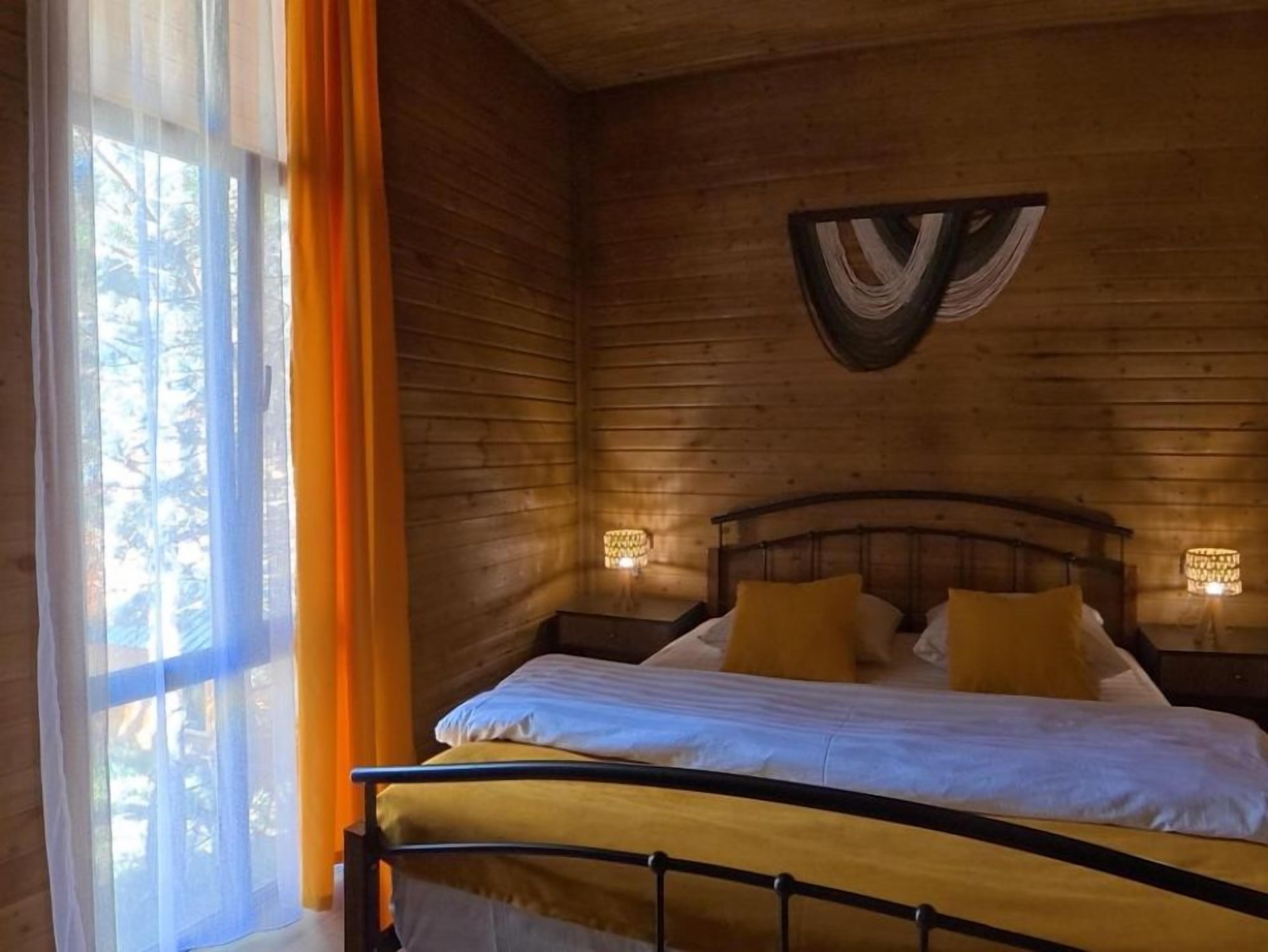 A wooden room with a bed, curtains, and wall-mounted lamps.