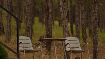 A secluded outdoor seating area with two metal chairs and a small round table, surrounded by tall trees.