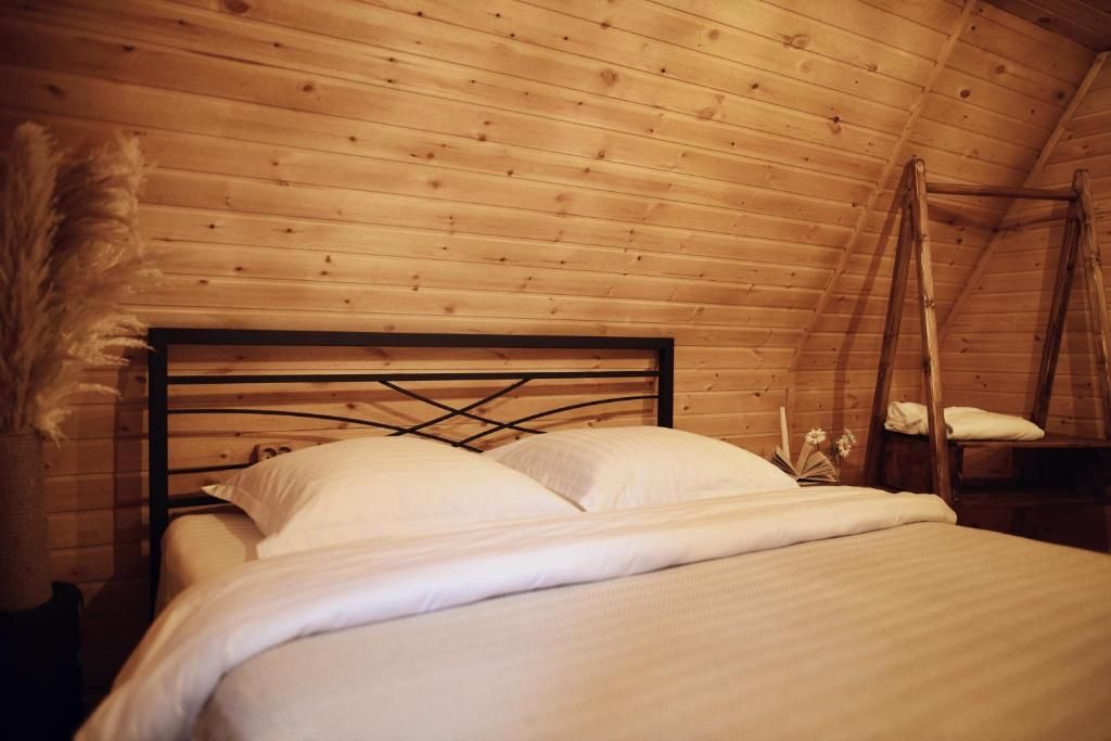 Un letto singolo con struttura in metallo e biancheria da letto bianca in una stanza con pareti in legno e soffitto spiovente.