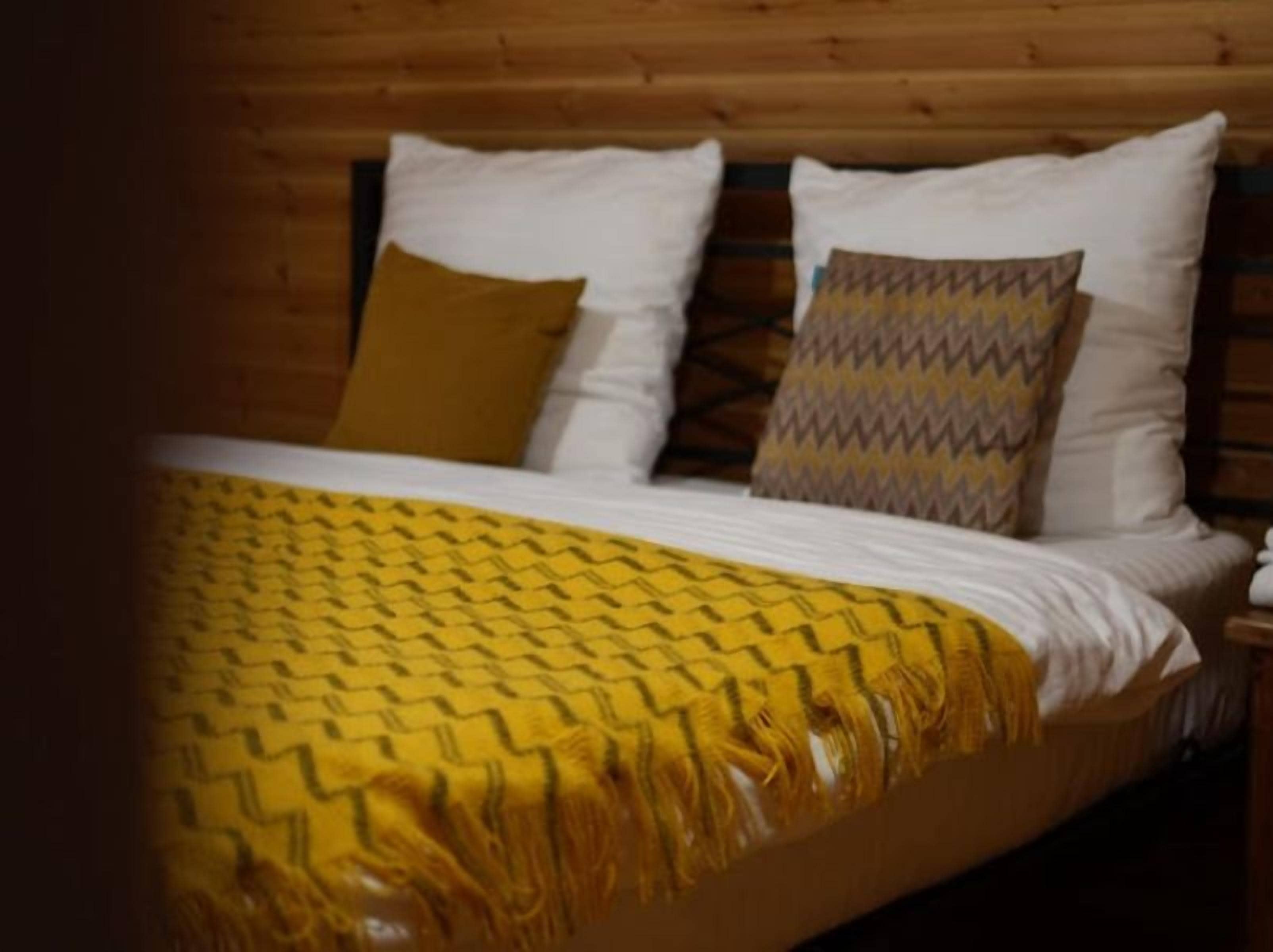 Una cama con una colcha amarilla estampada, almohadas blancas y un cabecero de madera.