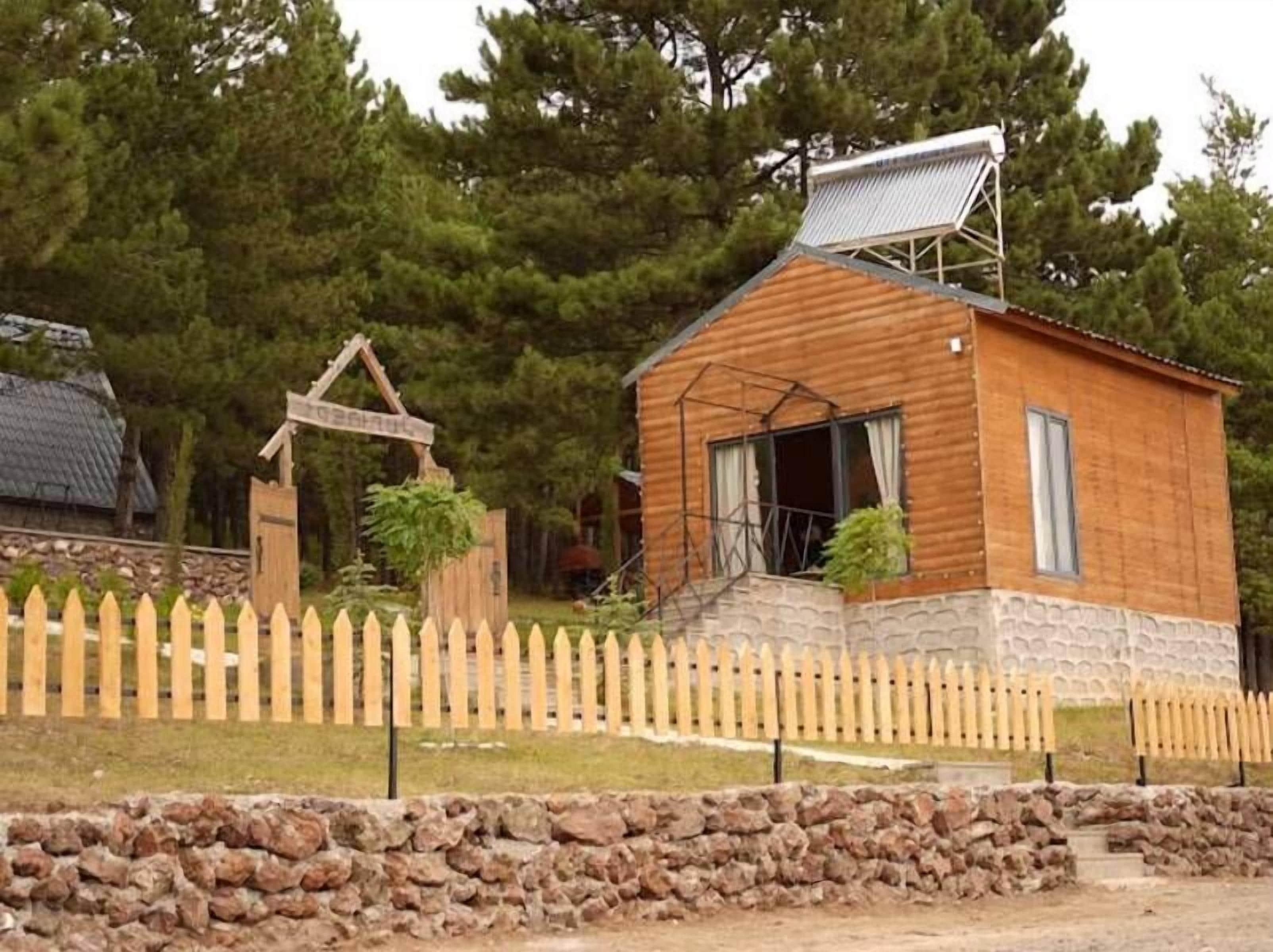 Una cabaña de madera con techo inclinado, un porche pequeño y un muro de piedra al frente.