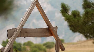 A wooden structure resembling a tent or shelter with a triangular roof, set against a natural landscape with trees and hills.
