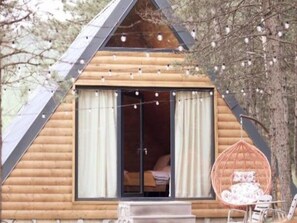 A wooden cabin with a triangular roof, a sliding glass door, and a hanging chair outside.