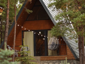 A wooden cabin with a sloped roof, a large window, and a chair outside. - Gyughak GuestHouse (Harzhis)