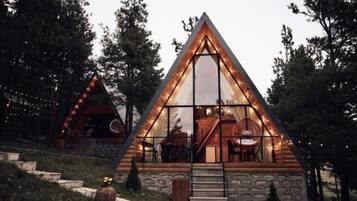 A cabin with a triangular roof, large windows, and a stone exterior.