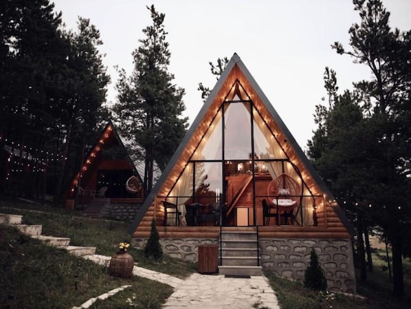 Una cabaña con techo triangular, ventanas amplias y fachada de piedra.