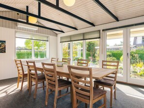 A dining area with a round table and chairs, large windows, and a view of greenery outside. - 8 Person Holiday Home in Bogense (Bogense)