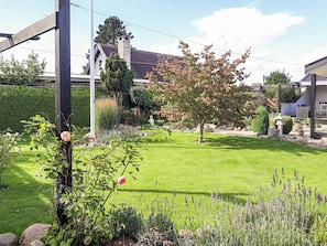 Un jardín bien cuidado con césped, diversas arbustas y un árbol de hojas color ocre.