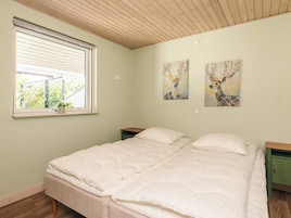 Un dormitorio con una cama, una ventana con persianas, una mesita pequeña y dos cuadros colgados en la pared.