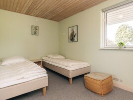 A bedroom with two beds, a window with blinds, and a small stool.