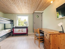 A room with bunk beds, a desk, a chair, a wardrobe, and a TV mounted on the wall.