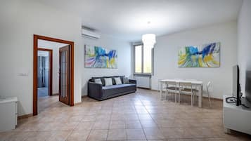 Una sala de estar con un sofá, una mesa de comedor con sillas y pinturas abstractas en las paredes.