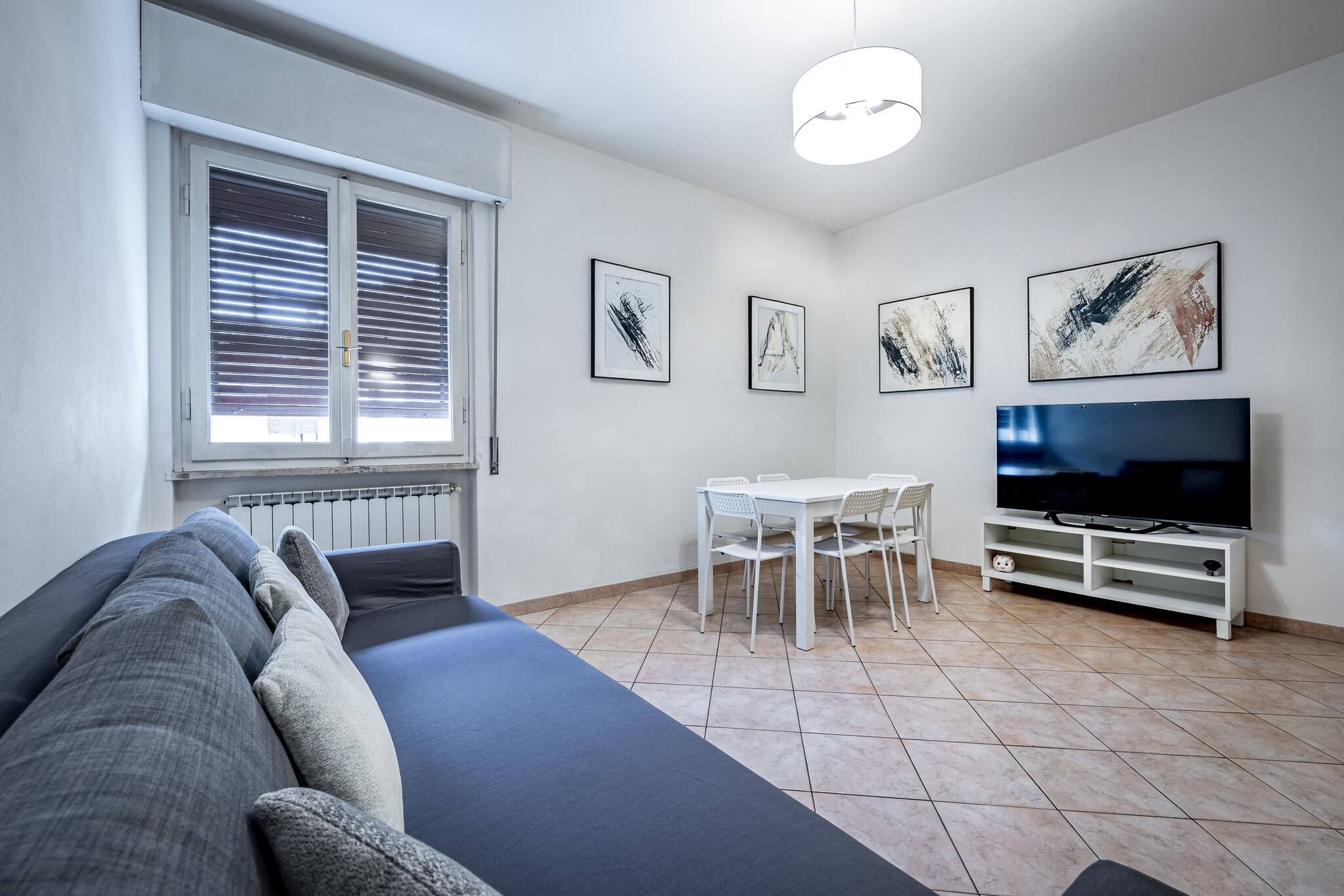 Una sala de estar con un sofá, un televisor, una mesa de comedor con sillas y obras de arte en las paredes.